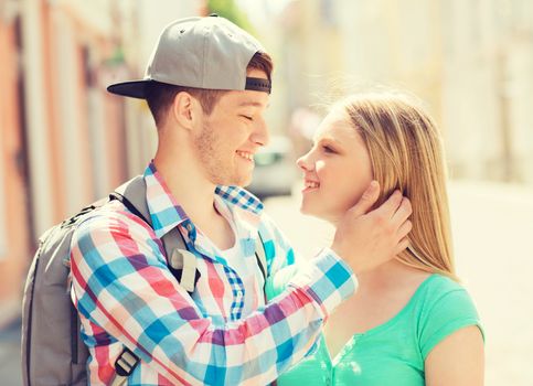 travel, vacation, love and friendship concept - smiling couple with backpack looking to each other in city