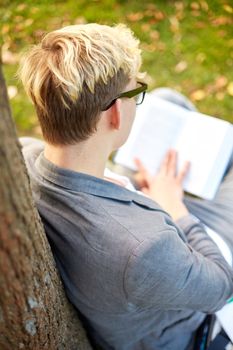 education, people and learning concept - teenage boy or young man reading book outdoors