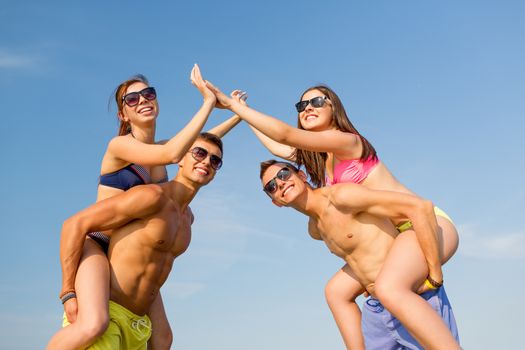 friendship, sea, gesture, holidays and people concept - group of smiling friends wearing swimwear having fun and making high five on beach
