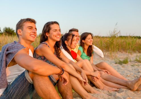 friendship, happiness, summer vacation, holidays and people concept - group of smiling friends sitting beach