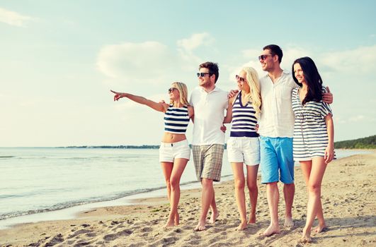 summer, holidays, sea, tourism and people concept - group of smiling friends in sunglasses walking on beach