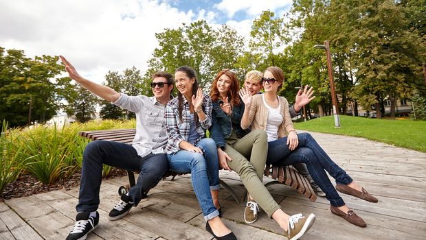 summer holidays, friendship, leisure and teenage concept - group of students or teenagers hanging out and waving hands at campus or park