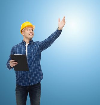 repair, construction, building, people and maintenance concept - smiling male builder or manual worker in helmet with clipboard pointing hand over blue background