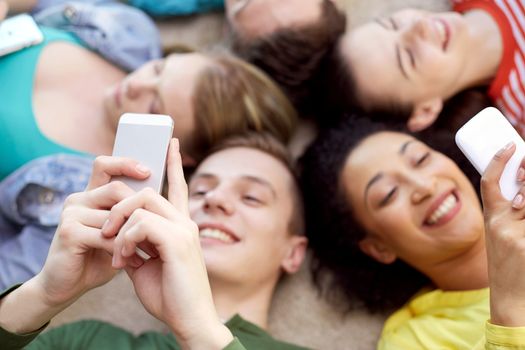 education, people and technology concept - close up of students or friends with smartphones lying on floor in circle