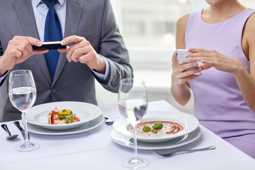 people, leisure, eating and technology concept - close up of couple with smartphones taking picture of food at restaurant