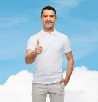 happiness, gesture and people concept - smiling man showing thumbs up over blue sky and cloud background