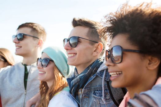 friendship, tourism, travel and people concept - group of happy teenage friends in sunglasses hugging outdoors