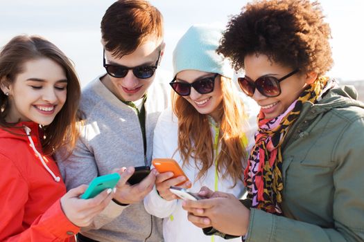 people, friendship, cloud computing and technology concept - group of smiling teenage friends with smartphone outdoors