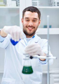 science, chemistry, technology, biology and people concept - young scientist mixing reagents from glass flasks and making test or research in clinical laboratory