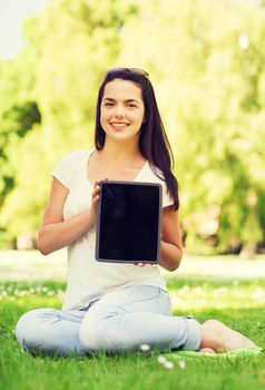 lifestyle, summer vacation, advertisement, technology and people concept - smiling young girl showing tablet pc screen and sitting in park