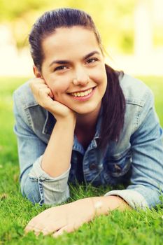 lifestyle, summer vacation, leisure and people concept - smiling young girl lying on grass in park