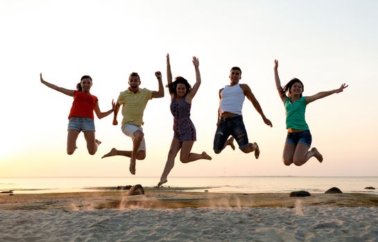 friendship, summer vacation, holidays, party and people concept - group of smiling friends dancing and jumping on beach