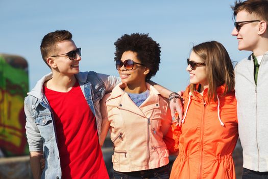 friendship, tourism, travel and people concept - group of happy teenage friends in sunglasses hugging and talking on city street