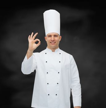 cooking, profession, gesture and people concept - happy male chef cook showing ok sign over black chalk board background