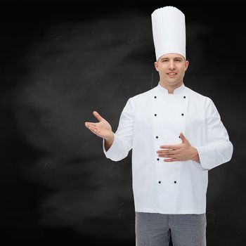 cooking, profession and people concept - happy male chef cook inviting over black chalk board background