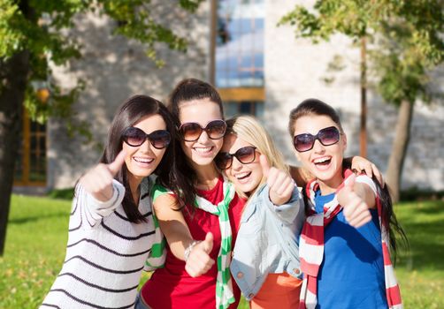 summer holidays, vacation and people concept - happy teenage girls in sunglasses or young students showing thumbs up over campus background