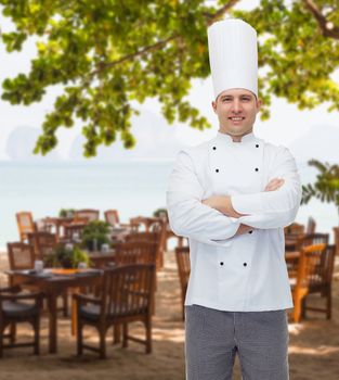 cooking, profession and people concept - happy male chef cook with crossed hands over restaurant lounge on beach