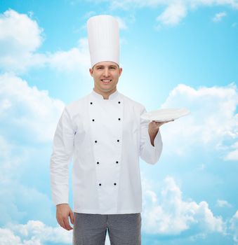 cooking, profession, advertisement and people concept - happy male chef cook showing something on empty plate over blue sky with clouds background