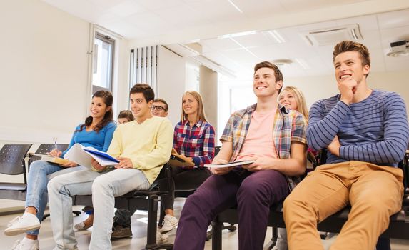 education, high school, teamwork and people concept - group of smiling students with notepads sitting in lecture hall