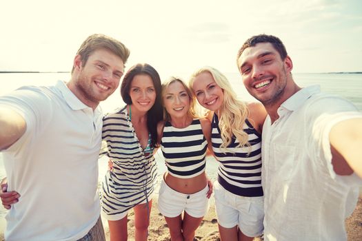 summer, sea, tourism, technology and people concept - group of smiling friends with camera on beach photographing and taking selfie