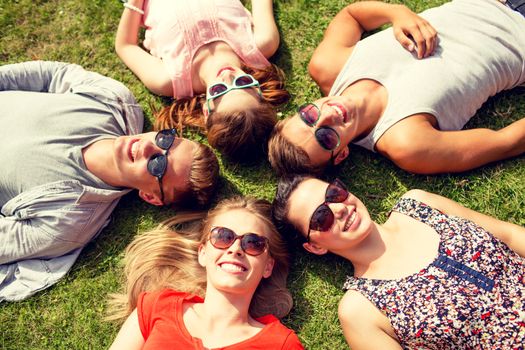 friendship, leisure, summer and people concept - group of smiling friends lying on grass in circle outdoors