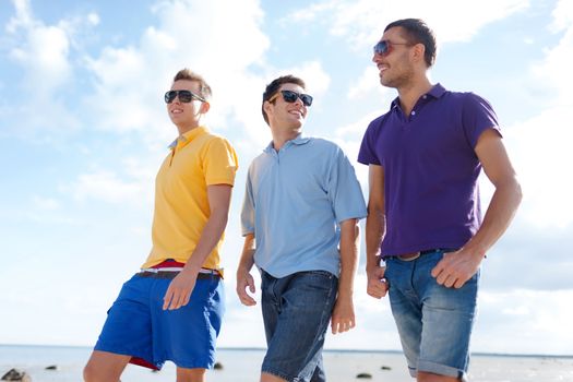 friendship, summer vacation, holidays and people concept - group of smiling male friends in sunglasses walking along beach