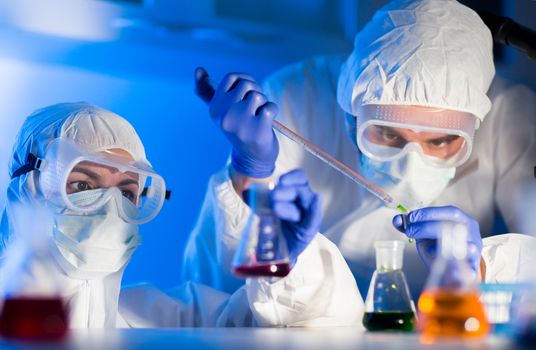 science, chemistry, biology, medicine and people concept - close up of young scientists with pipette and flasks making test or research in clinical laboratory