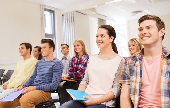 education, high school, teamwork and people concept - group of smiling students with notepads sitting in lecture hall