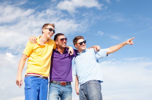 friendship, summer vacation, holidays and people concept - group of smiling male friends in sunglasses pointing finger on beach