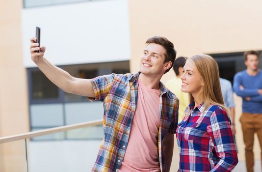 friendship, people, technology and education concept - group of smiling students with smartphone taking selfie outdoors