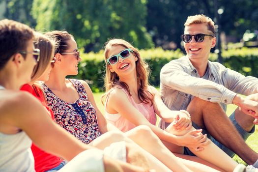 friendship, leisure, summer and people concept - group of smiling friends outdoors sitting on grass in park