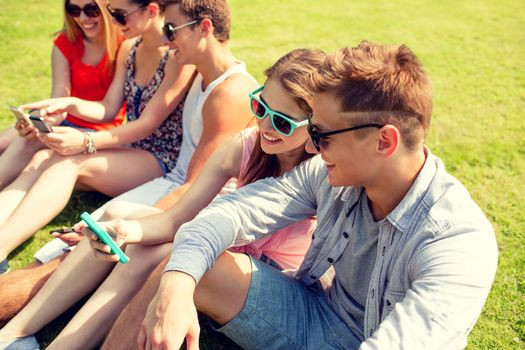 friendship, leisure, summer, technology and people concept - group of smiling friends with smartphone sitting on grass and making selfie in park