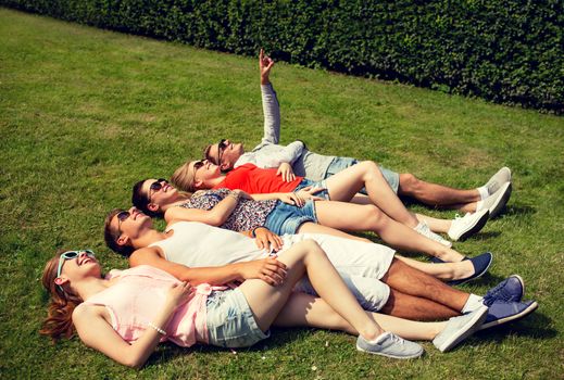 friendship, leisure, summer and people concept - group of smiling friends lying on grass outdoors