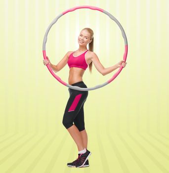 fitness, sport, people and healthcare concept - young sporty woman exercising with hula hoop over yellow striped background