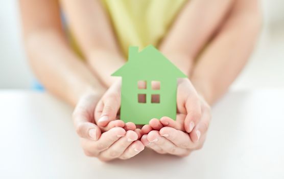 people, charity, family and home concept - close up of woman and girl holding green paper house cutout in cupped hands