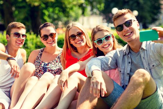 friendship, leisure, summer, technology and people concept - group of smiling friends with smartphone making selfie in park