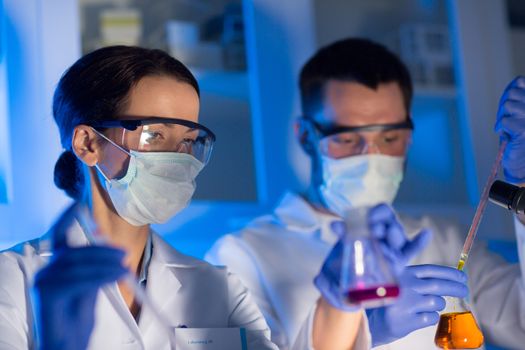 science, chemistry, biology, medicine and people concept - close up of young scientists with pipette and flasks making test or research in clinical laboratory