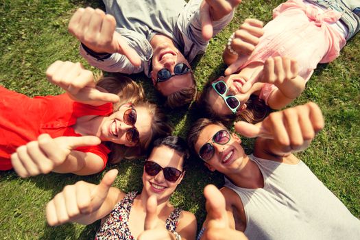 friendship, leisure, summer, gesture and people concept - group of smiling friends lying on grass in circle and showing thumbs up outdoors