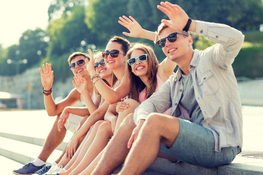 friendship, leisure, summer, gesture and people concept - group of smiling friends sitting on city square