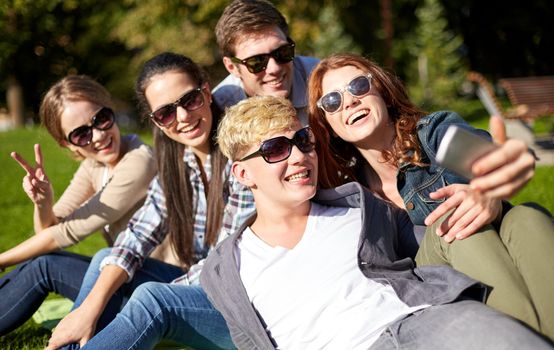 summer, technology, education and teenage concept - group of happy students or teenagers with smarphone taking selfie at campus