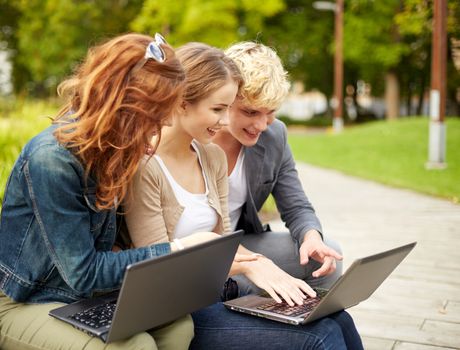 summer, education, technology and people concept - group of students or teenagers with laptop computers sitting on bench outdoors