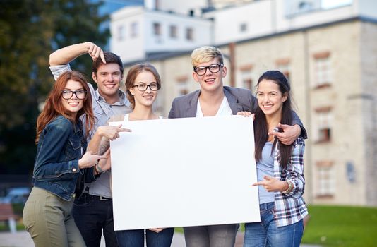 education, campus, friendship and people concept - group of happy teenage students holding big white blank billboard