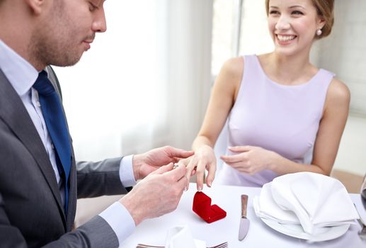 couple, love, engagement and holiday concept - close up of man putting ring to his fiance finger at restaurant