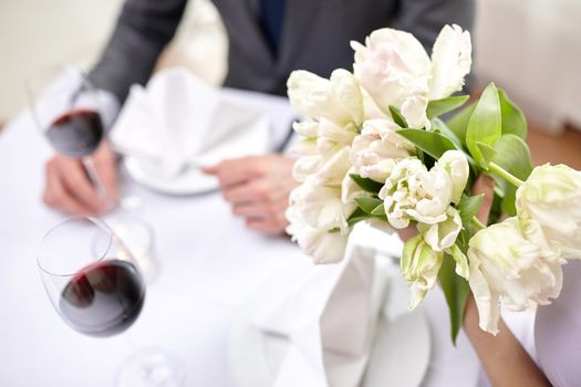 restaurant, people, celebration and holiday concept - close up of young couple with tulip flowers and glasses of red wine at restaurant