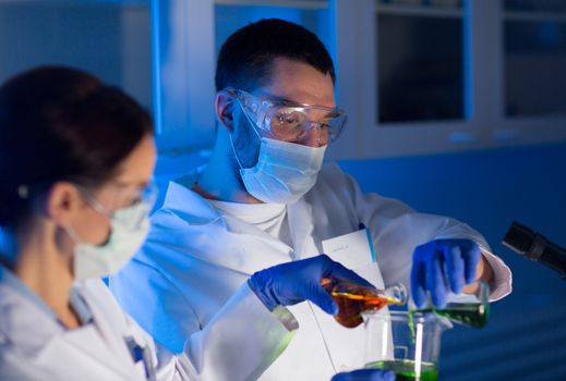 science, chemistry, biology, medicine and people concept - close up of young scientists with pipette and flasks making test or research in clinical laboratory