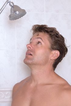 Closeup shirtless Caucasian man ready to take shower staring up at shower head but no water comes out