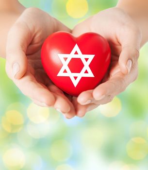 religion, christianity, jewish community and charity concept - close up of female hands holding red heart with star of david symbol over green lights background