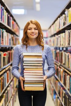 people, knowledge, education and school concept - happy student girl or young woman with stack of books in library