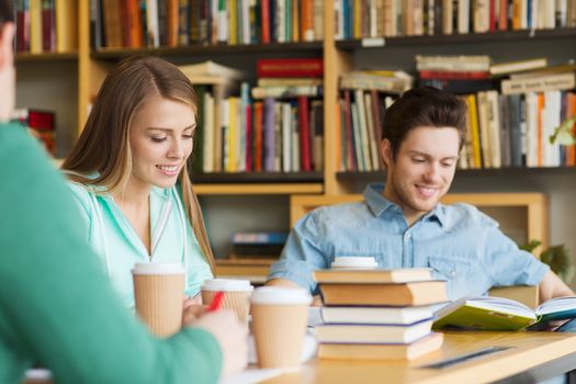 people, knowledge, education and school concept - group of happy students reading books, drinking coffee and preparing to exam in library