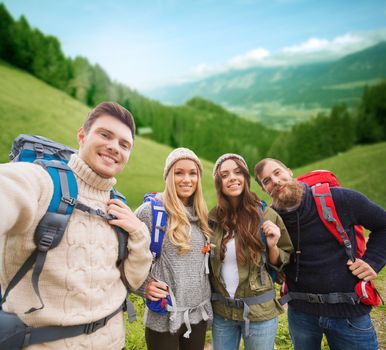 adventure, travel, tourism, hike and people concept - group of smiling friends with backpacks making selfie over alpine hills background